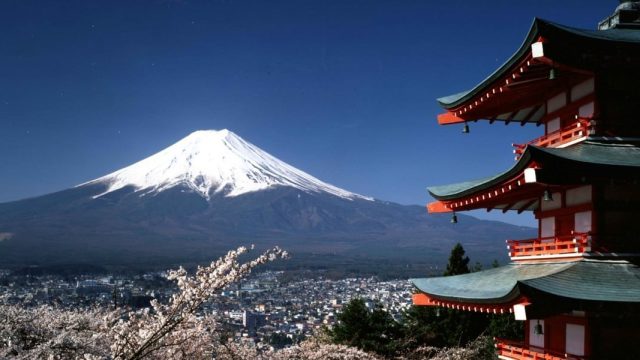 Japón. Japón Vista del Monte Fuji desde un zona de templos, uno de los cuales se puede ver parcialmente a la derecha, y unas ramas de cerezos en flor en primer término abajo, tapando las vistas de la ciudad a los pies del monte, en Japón.